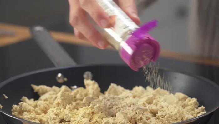 Añadir los condimentos: sal fina, ajo en polvo, 1.5 cucharadas de levadura nutricional, pimienta negra recién molida, un poco de cúrcuma molida y un chorro de leche de soja sin azúcar.