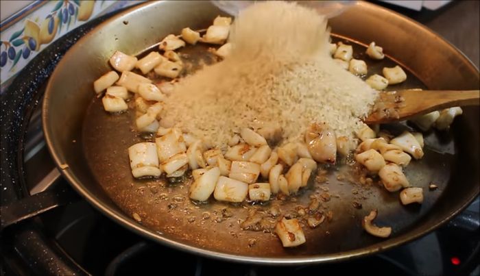 Añadimos el arroz a la sartén con la sepia y los calamares y removemos durante un minuto.