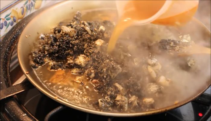 Agregamos el caldo de pescado (caliente y colado) – el doble de caldo que de arroz – y movemos para que la consistencia sea igual en todo el arroz.