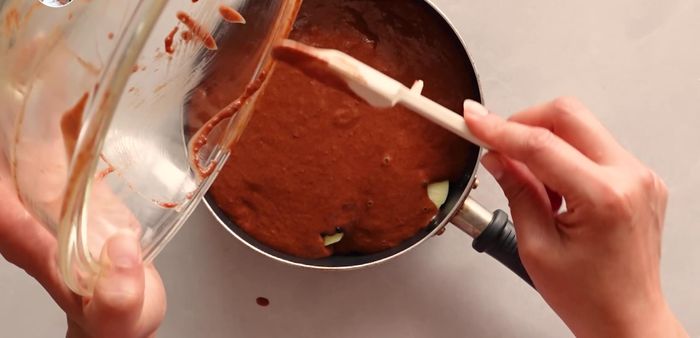Vierte la mezcla sobre las manzanas en la sartén. Da unos ligeros golpes para distribuir la mezcla y eliminar burbujas de aire.
