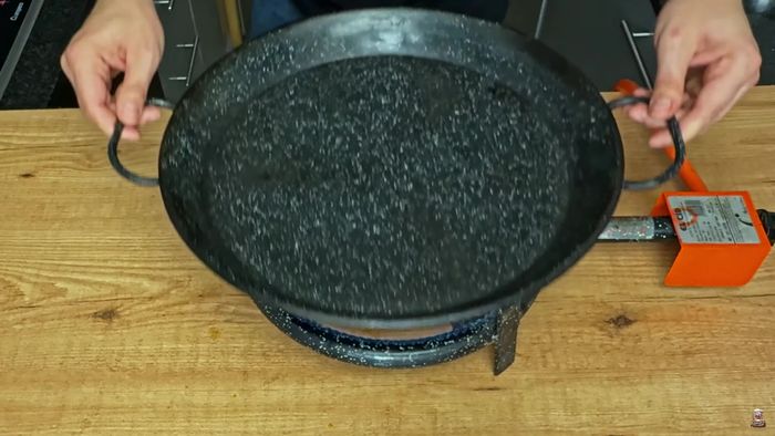 Encendemos el fuego y calentamos la paella. Ponemos papel sulfurizado y añadimos la dorada con la piel hacia abajo.
