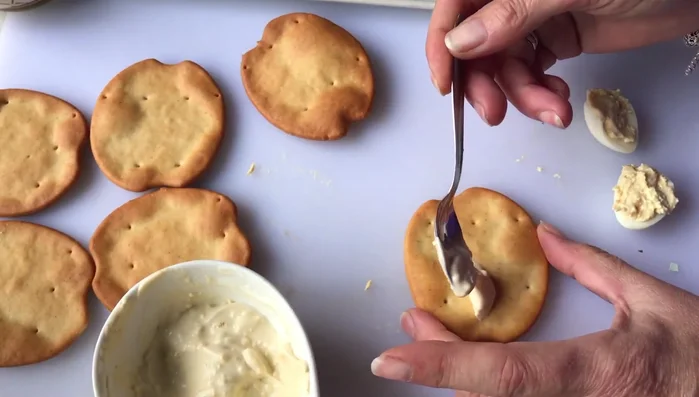Untar un poco de la mezcla de mayonesa y yema en las marineras de aceite. Esto servirá como base y pegamento para los huevos.