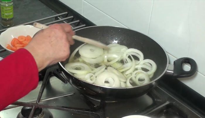 Bajar el fuego. Añadir la cebolla y las zanahorias cortadas en rodajas, las bolitas de pimienta, la hojita de laurel partida por la mitad y los ajos con piel. Remover.