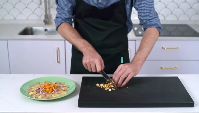Añadir rodajas finas de cebolla roja, kikos machacados (o choclo) y cilantro fresco picado. Salar el pescado.