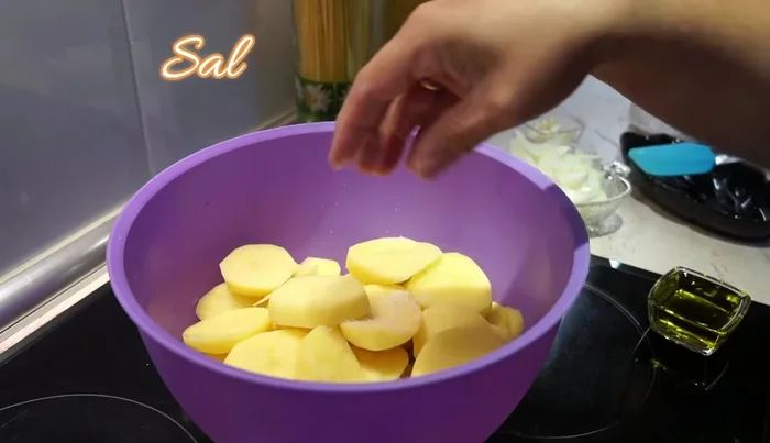 Prepara la guarnición: Corta 5 patatas en rodajas gruesas, sazona con sal y añade una cebolla cortada en juliana, 5-7 dientes de ajo, pimienta y 4 cucharadas de aceite de oliva. Mezcla bien.