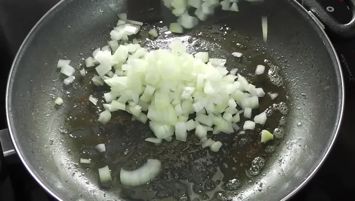 Agregar un poco más de aceite a la paellera, añadir la cebolla y el pimiento, una pizca de sal y cocinar a fuego medio hasta que estén tiernos.