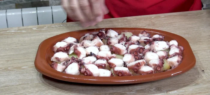 Colocar las patatas en una fuente, añadir el pulpo encima y sazonar con sal gorda, pimentón dulce y pimentón picante.
