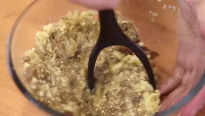 Utilizando un tenedor, un pisa papas o una batidora, triturar la pulpa de berenjena hasta obtener una textura deseada. Incorporar la mezcla de ajo y especias.