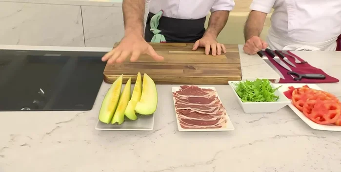 Limpiar el melón. Pelar y cortar el tomate en dados pequeños. Picar la cebolla morada, las aceitunas y las hierbas aromáticas (menta y albahaca).